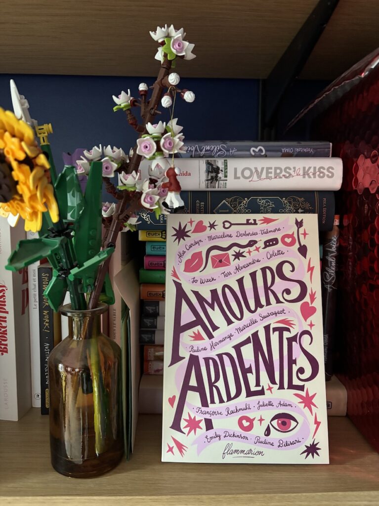 Un exemplaire du livre, posé sur une étagère à côté d'un bouquet de fleurs Lego dans une bouteille en verre ambré. Derrière le livre, une pile de mangas dont le titre "Lover's Kiss" sort du lot.